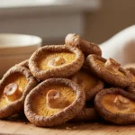 A close-up, overhead shot showcases golden-brown, crispy shiitake mushroom air fryer pieces arranged artfully on a rustic wooden board.